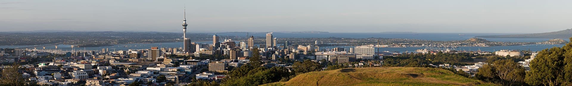Auckland travel planning photo showing The Skyline of Auckland City, in the foreground a part of Mt. Eden is visible, left in the background is the Auckland Harbour Bridge. Panora